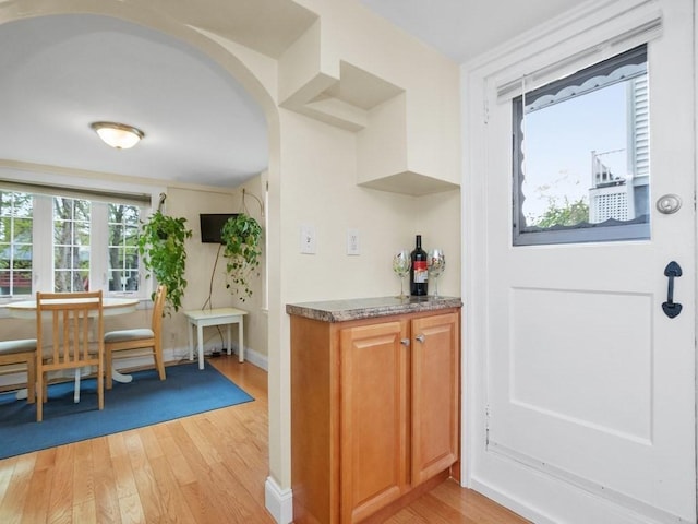 bar featuring arched walkways, baseboards, and light wood finished floors