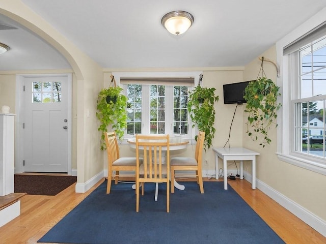 dining room with baseboards, arched walkways, and wood finished floors