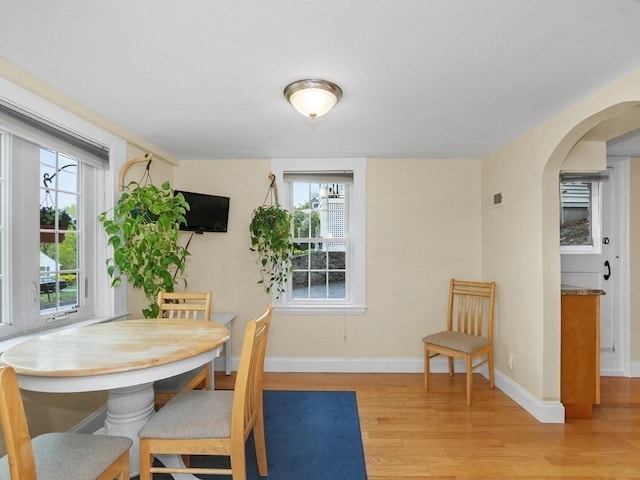 dining room with a healthy amount of sunlight, arched walkways, baseboards, and light wood-style flooring