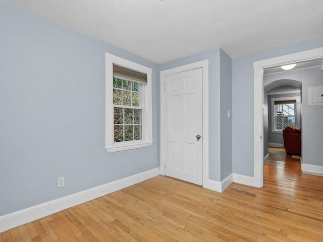 unfurnished bedroom with light wood-type flooring, arched walkways, baseboards, and a closet