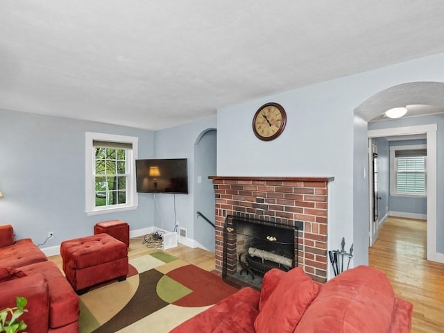 living area with arched walkways, a brick fireplace, wood finished floors, and a wealth of natural light