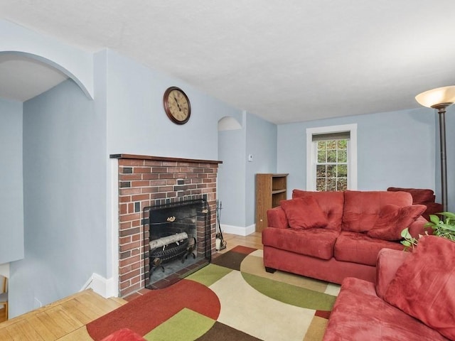 living area with baseboards, a brick fireplace, arched walkways, and wood finished floors