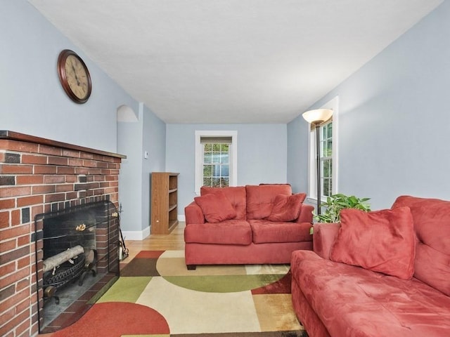 living room featuring baseboards, a brick fireplace, and wood finished floors