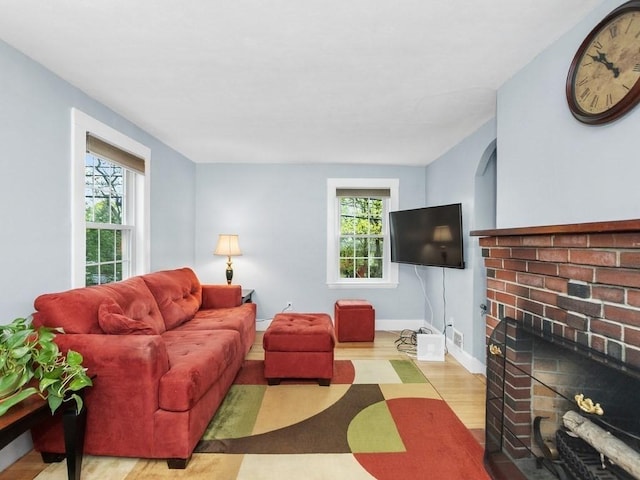 living area with baseboards, a brick fireplace, and wood finished floors