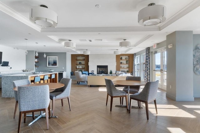 dining area with a tray ceiling, a fireplace, ornamental molding, and light parquet flooring