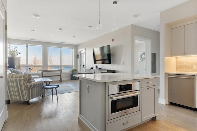 kitchen featuring light hardwood / wood-style flooring, appliances with stainless steel finishes, a center island, decorative backsplash, and decorative light fixtures