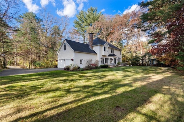 view of front of house featuring driveway, a front lawn, an attached garage, and a chimney