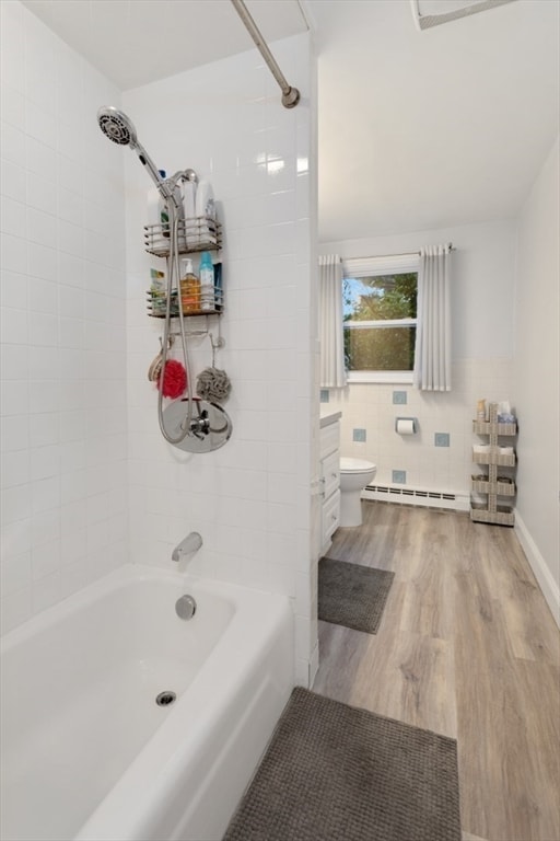 bathroom featuring toilet, tiled shower / bath combo, baseboard heating, tile walls, and hardwood / wood-style floors