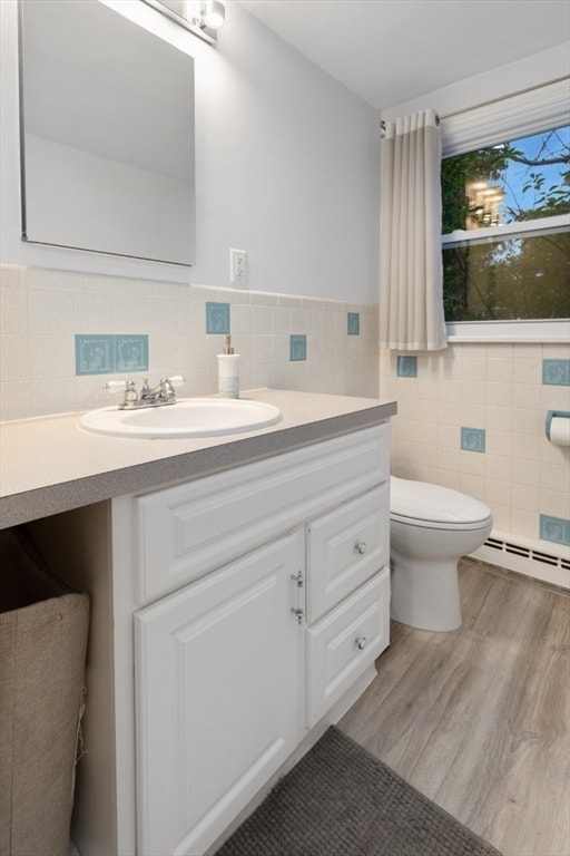 bathroom featuring vanity, wood-type flooring, a baseboard heating unit, tile walls, and toilet