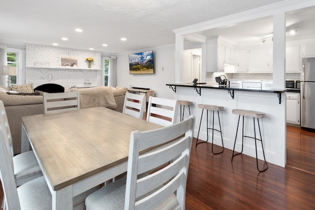 dining space featuring ornamental molding, a healthy amount of sunlight, a large fireplace, and dark hardwood / wood-style flooring