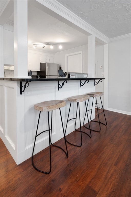 kitchen featuring white cabinets, stainless steel refrigerator, dark hardwood / wood-style flooring, crown molding, and a breakfast bar area