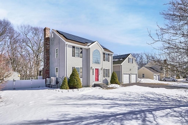 view of front of house with roof mounted solar panels, fence, a chimney, and a gate