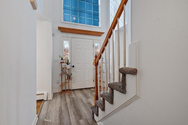 entryway featuring a towering ceiling, a baseboard heating unit, wood finished floors, baseboards, and stairs