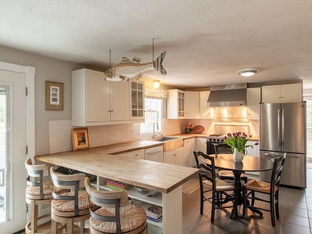 kitchen featuring a sink, appliances with stainless steel finishes, glass insert cabinets, tile patterned flooring, and wall chimney range hood