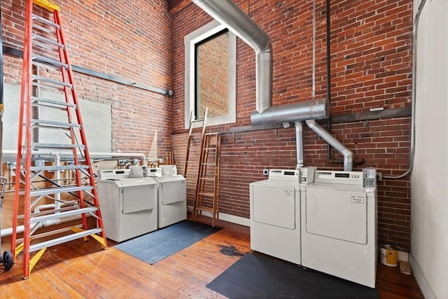 shared laundry area with washer and dryer, brick wall, baseboards, and wood-type flooring
