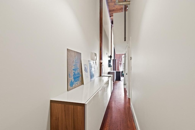 corridor with dark wood-type flooring, baseboards, and a towering ceiling