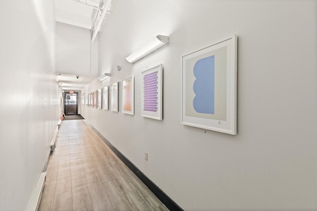 hall featuring baseboards, wood finished floors, and a towering ceiling