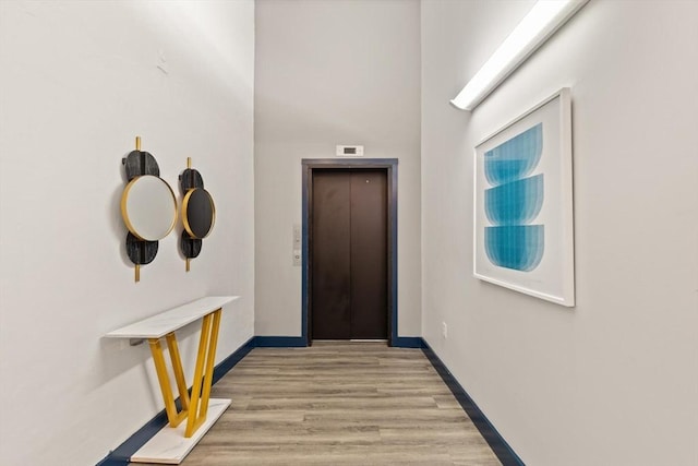 corridor with elevator, baseboards, and light wood-type flooring