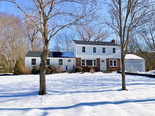 view of front facade featuring a garage, brick siding, a chimney, and an outbuilding