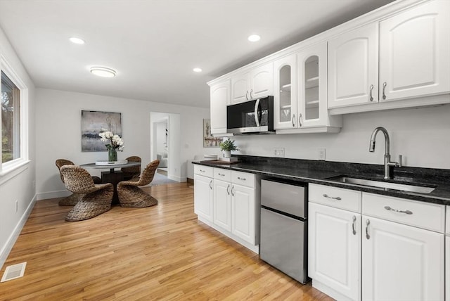 kitchen featuring visible vents, white cabinets, freestanding refrigerator, light wood-type flooring, and a sink