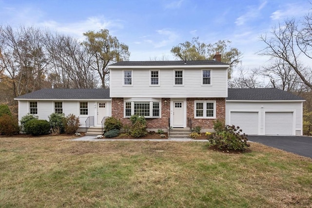 colonial house with driveway, a chimney, an attached garage, and a front yard