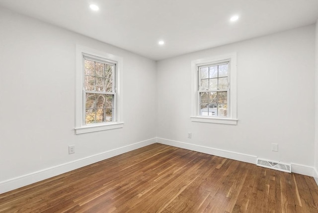 spare room featuring a healthy amount of sunlight, visible vents, baseboards, and wood finished floors