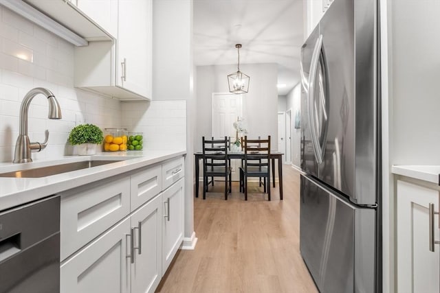 kitchen with sink, pendant lighting, white cabinets, and stainless steel refrigerator