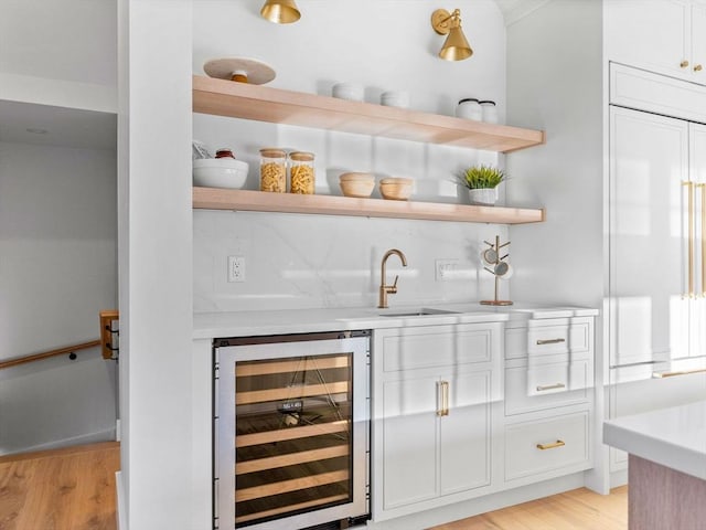 bar featuring paneled built in fridge, sink, light hardwood / wood-style floors, white cabinetry, and beverage cooler