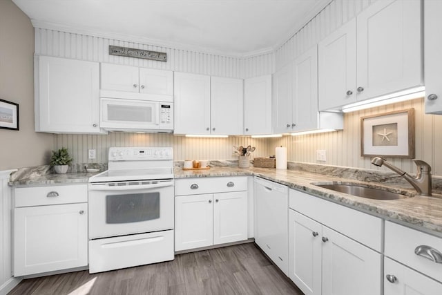 kitchen with wood finished floors, white appliances, light stone countertops, white cabinets, and a sink