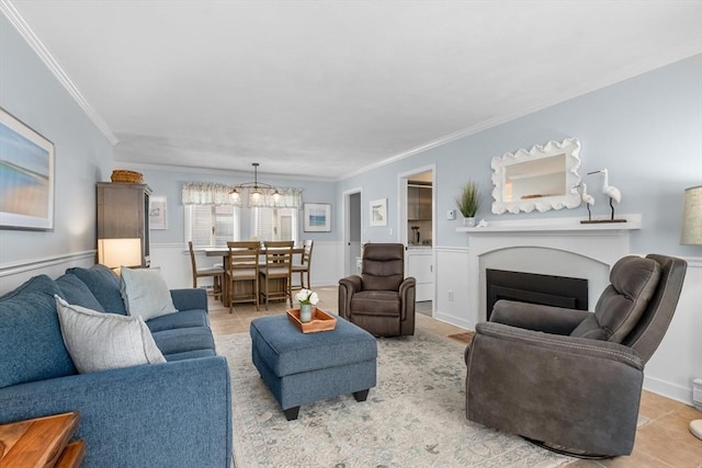 living room with crown molding, a wainscoted wall, a fireplace, and a chandelier