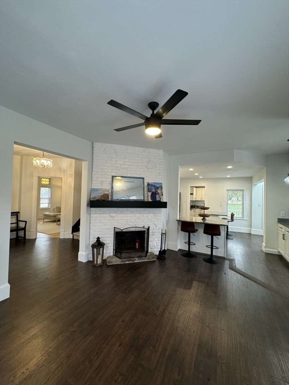 living room with ceiling fan with notable chandelier, a fireplace, and dark hardwood / wood-style flooring