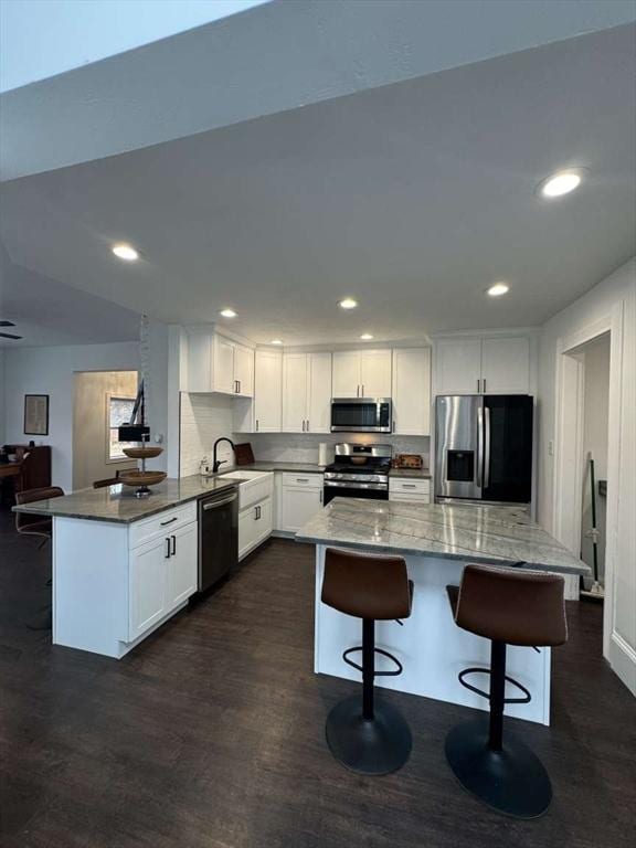 473 Massasoit Rd, Worcester, MA 01604 - kitchen with dark stone countertops, a breakfast bar, white cabinetry, dark wood-type flooring, and appliances with stainless steel finishes