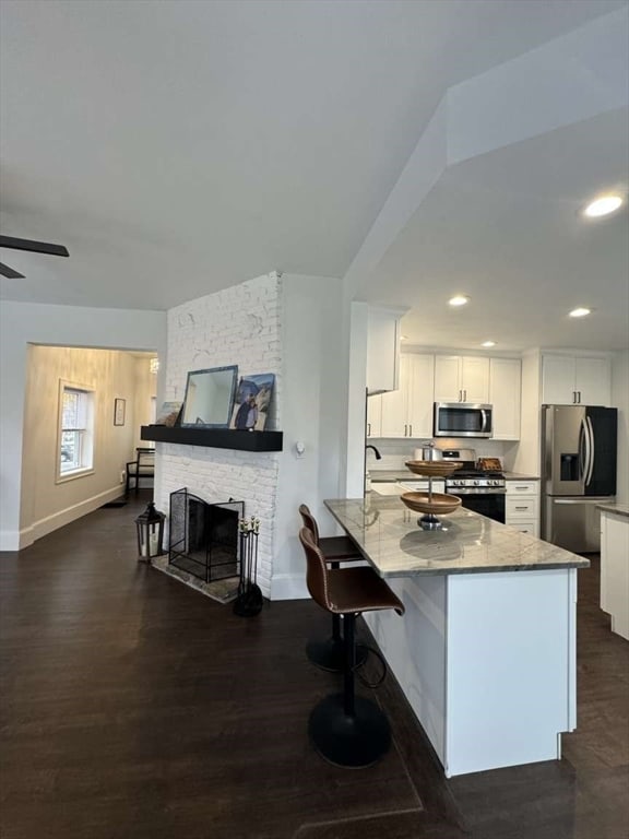 kitchen with a stone fireplace, dark wood-type flooring, white cabinets, appliances with stainless steel finishes, and light stone counters