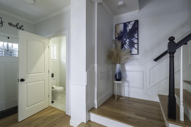 bathroom featuring crown molding, a decorative wall, toilet, wood finished floors, and wainscoting