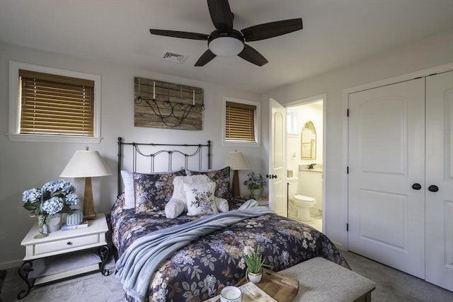carpeted bedroom with ensuite bath, visible vents, a closet, and a ceiling fan