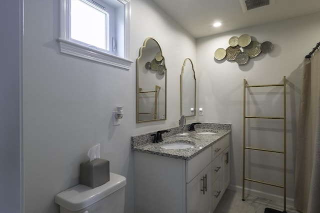 bathroom featuring toilet, double vanity, a sink, and visible vents