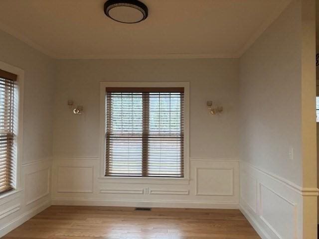 unfurnished room featuring light wood-style flooring, plenty of natural light, and a wainscoted wall