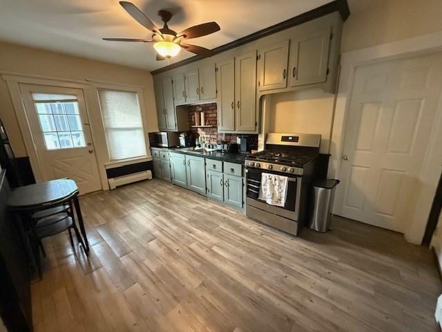 kitchen with sink, ceiling fan, a baseboard heating unit, light hardwood / wood-style floors, and stainless steel range with gas cooktop