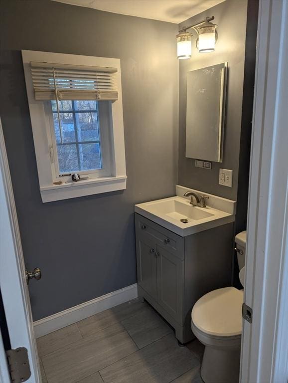half bathroom featuring baseboards, toilet, and vanity