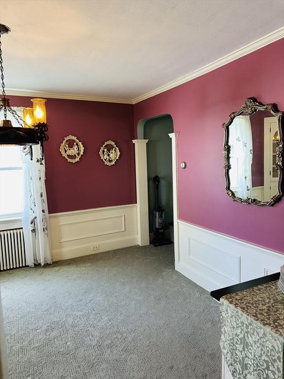70 Sherman St, Quincy, MA 02170 - spare room featuring arched walkways, a wainscoted wall, carpet flooring, ornamental molding, and a decorative wall