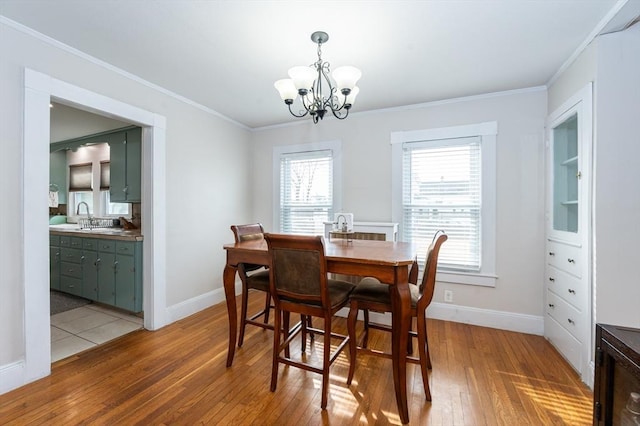 dining room featuring light wood finished floors, a chandelier, baseboards, and ornamental molding