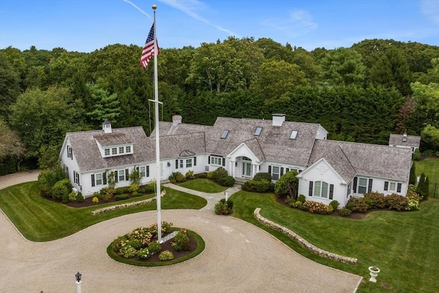 view of front facade featuring a forest view, a front lawn, curved driveway, and a chimney