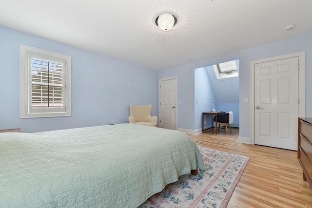 bedroom with light wood finished floors, vaulted ceiling with skylight, and baseboards