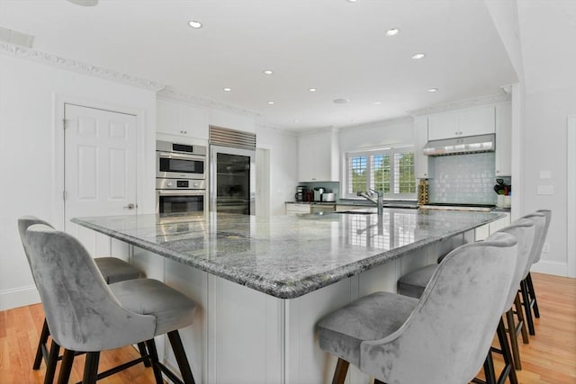 kitchen featuring double oven, built in fridge, white cabinets, light wood-type flooring, and backsplash