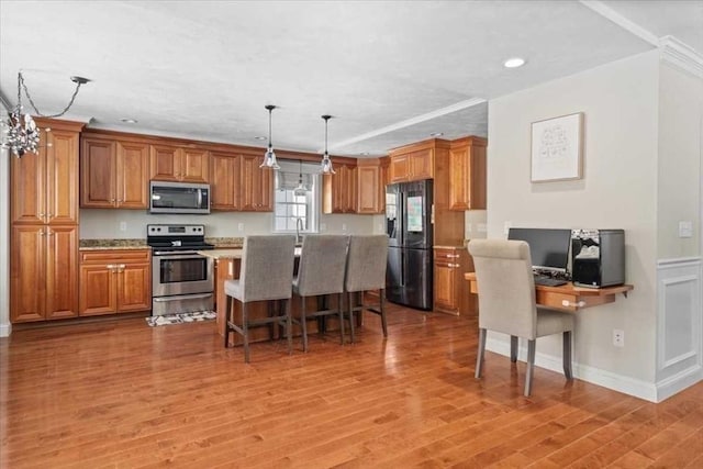 kitchen featuring light wood-style flooring, appliances with stainless steel finishes, brown cabinets, and a breakfast bar area