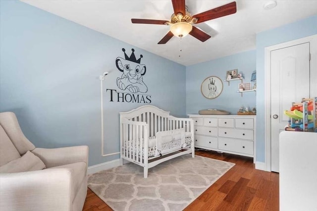 bedroom featuring a nursery area, ceiling fan, wood finished floors, and baseboards