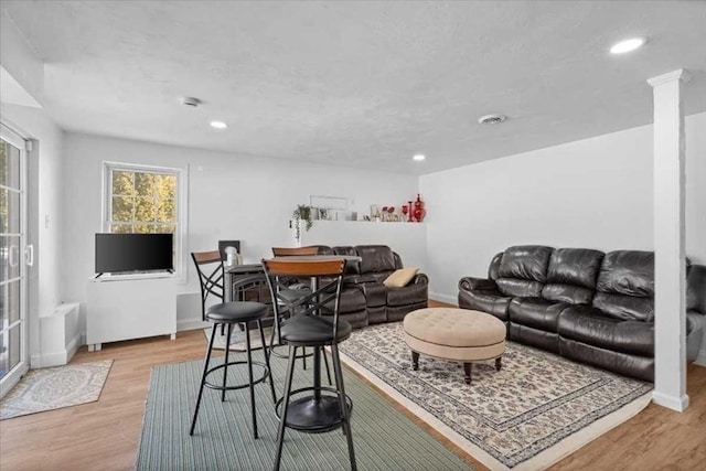 living area featuring light wood finished floors, baseboards, visible vents, and ornate columns