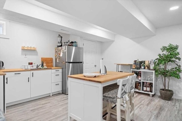 kitchen with wooden counters, light wood-style flooring, freestanding refrigerator, and white cabinetry