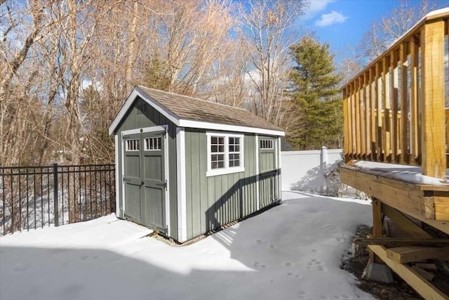 snow covered structure with a storage shed, an outdoor structure, and fence