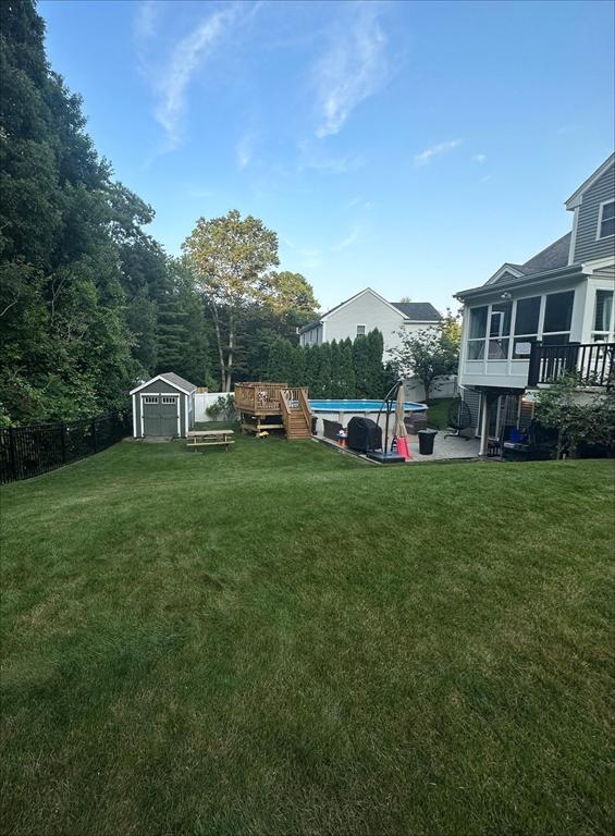 view of yard with an outbuilding, a storage shed, a sunroom, fence, and an outdoor pool